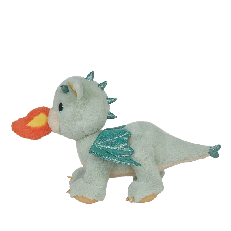 The Olli Ella Dinkum Dragon - Blaze - Green is a light green plush dragon toy with blue wings and spikes, standing on four legs and featuring a magnetic mouth that breathes an orange and yellow fabric flame.