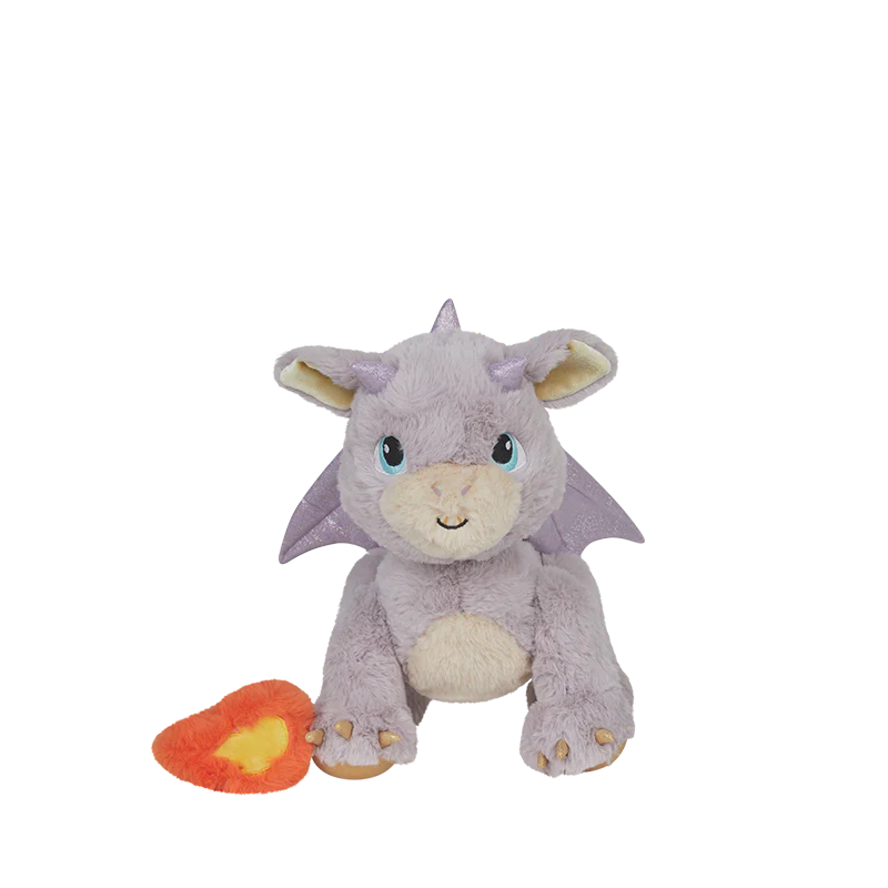 The Olli Ella Dinkum Dragon - Flare - Lavender, a plush purple dragon with blue eyes and a friendly smile, sits beside a red and yellow heart-shaped accessory, making the perfect magical companion on a white background.