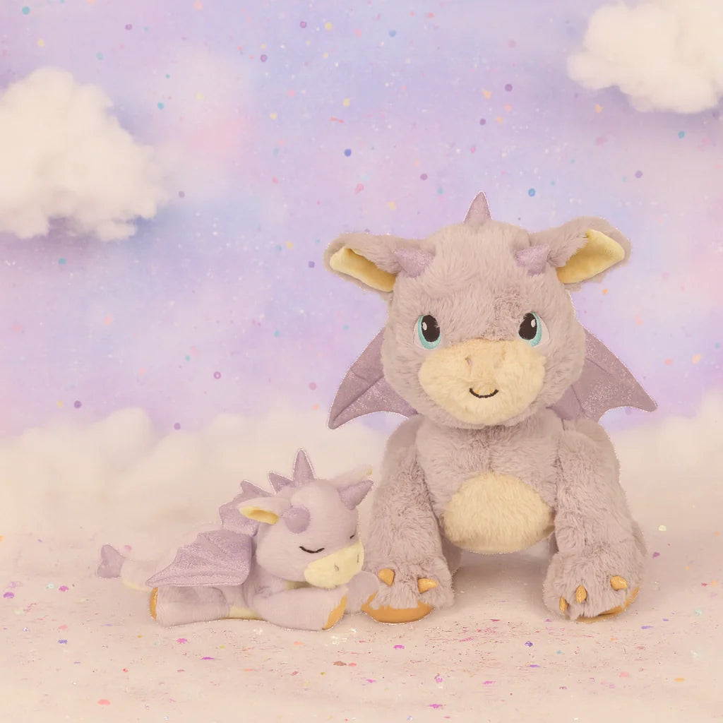 Two plush Olli Ella Dinkum Dragon - Flare - Lavender toys sit on a soft, pastel surface with dreamy clouds and a starry lavender sky—one upright and smiling, the other peacefully asleep, like magical companions in an enchanting world.