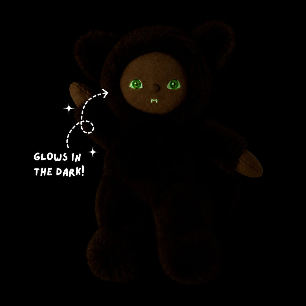 An Olli Ella Dinky Dinkum Doll - Wesley Werewolf with dark fur, glowing green eyes, and fangs, featuring a dashed arrow pointing to its paw with text that reads “GLOWS IN THE DARK!”.