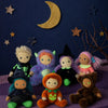 Seven small Halloween stuffed animal dolls, including an Olli Ella Dinky Dinkum Doll - Miles Monster, a pumpkin, and witches, arranged on a purple blanket against a backdrop with a moon and stars.
