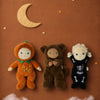 Three Dinkum Dolls on a brown surface, including an Olli Ella Dinky Dinkum Doll - Scully Skeleton, one in a pumpkin outfit, and one in a fuzzy brown costume, surrounded by cutout stars and a moon.