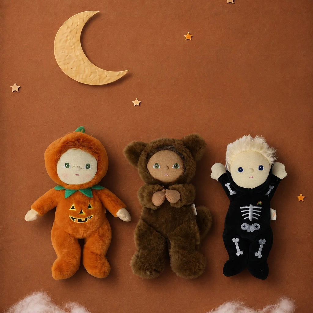 Three dolls, including an Olli Ella Dinky Dinkum Doll - Wesley Werewolf dressed as a werewolf, alongside two others in pumpkin and skeleton costumes, positioned beneath a crescent moon and stars on a brown background.