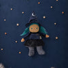 An Olli Ella Dinky Dinkum Doll - Winnie Witch dressed in a pointed hat, blue hair, and a starry skirt, surrounded by small wooden stars on a dark blue background.