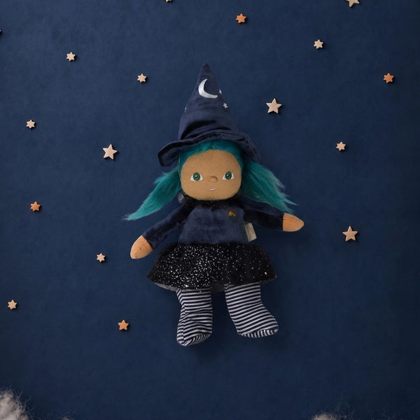 An Olli Ella Dinky Dinkum Doll - Winnie Witch dressed in a pointed hat, blue hair, and a starry skirt, surrounded by small wooden stars on a dark blue background.