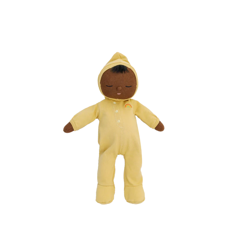 Olli Ella Dozy Dinkum - Mini: a plush doll with brown skin, closed eyes, black hair, and a calm face, dressed in a yellow hooded onesie with a rainbow motif. Made from soft cotton—perfect as baby's first toy. Shown on a plain white background.