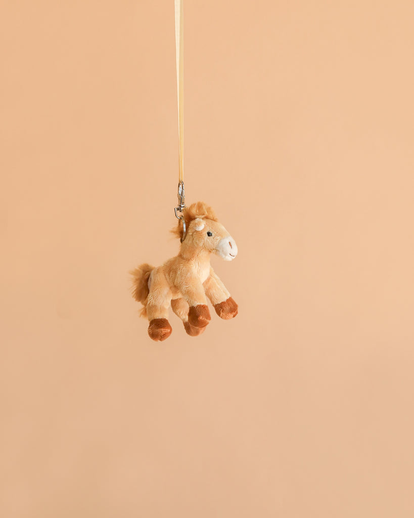 The Bukowski - Pony Sugar Bag Charm, a small plush horse toy designed as an adorable pony accessory, hangs by a yellow strap against a plain beige background.