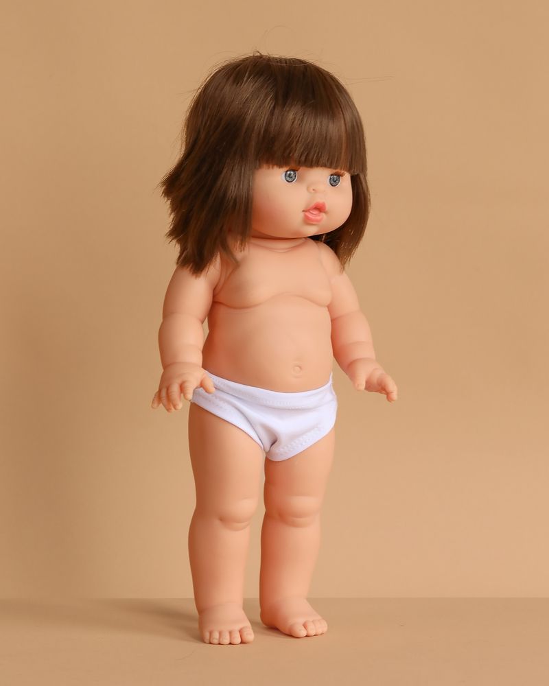The Minikane Standing Doll (14") - Chléa, made in Spain, features short brown hair and blue eyes, posed upright in white underwear against a plain beige background. Clothing sold separately.