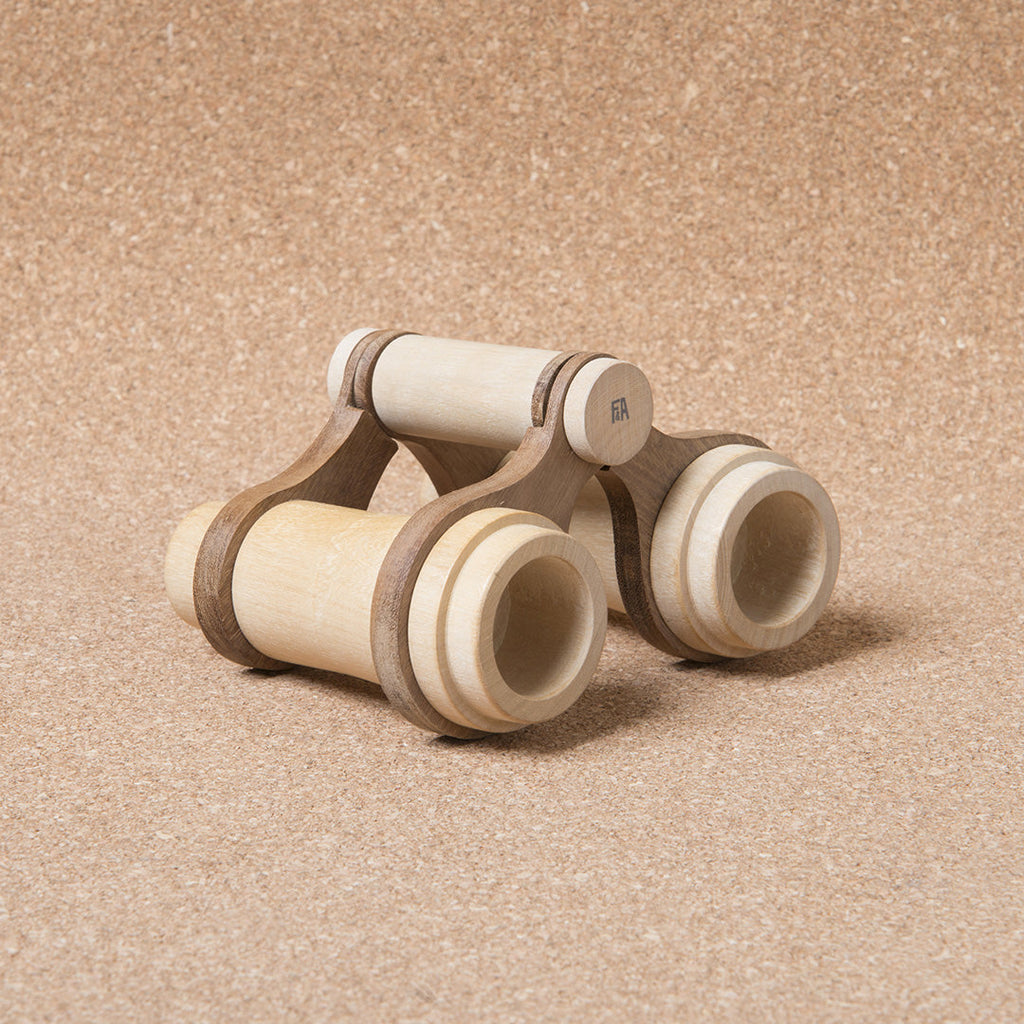 Heirloom quality Wooden Binoculars For Pretend Play made from solid beech wood, positioned on a textured beige background. The toy has a simple, child-friendly design, with cylindrical bodies and a connecting bridge.