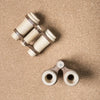 A top-down view of two different sets of Wooden Binoculars For Pretend Play on a sandy background. The top pair is vintage with extendable tubes, and the bottom pair is modern and compact.