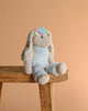 Steiff Hoppie Rabbit in Ski Outfit, 12 inches, is a light blue and gray plush bunny with floppy ears. Wearing a shiny iridescent sleep mask, this winter stuffed animal stands out against the plain light brown background.