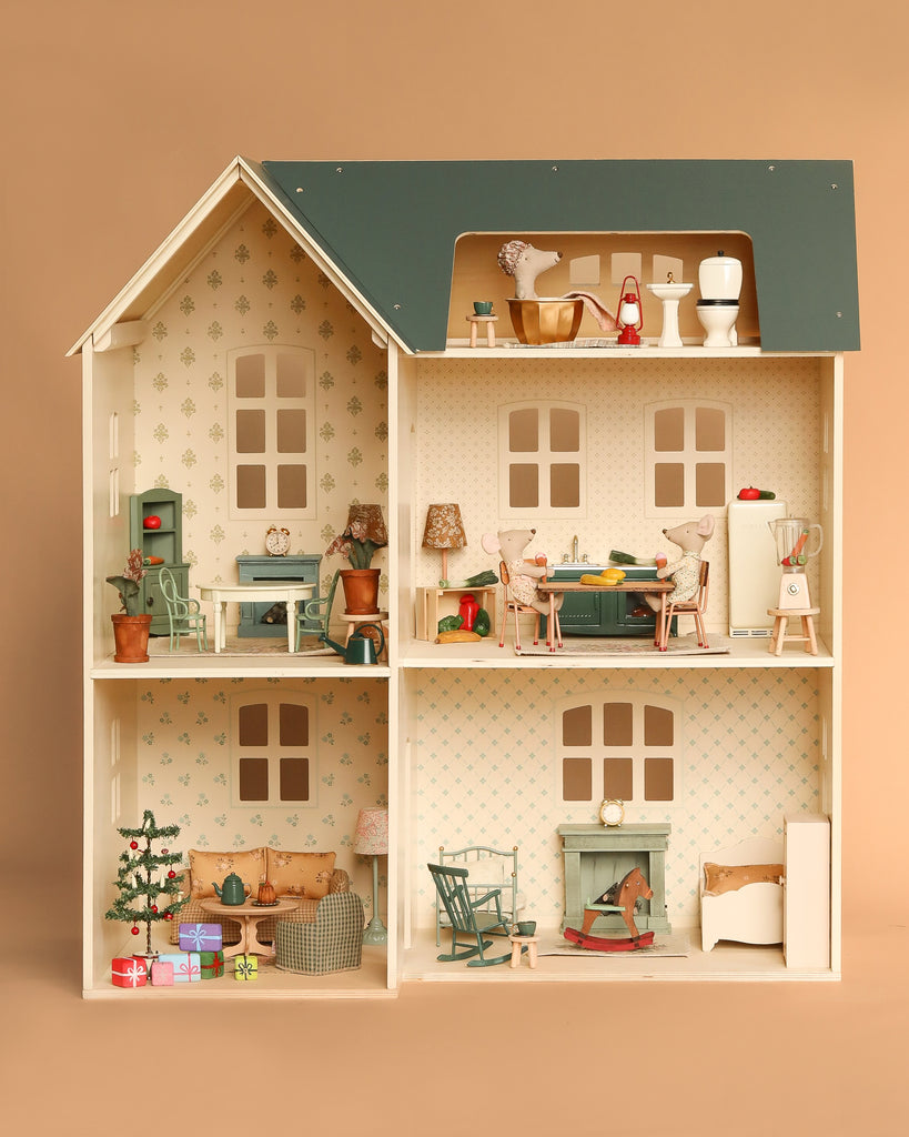 The Maileg Fully Furnished Holiday Dollhouse Set features an open-front beige house with four decorated rooms, complete with charming furniture, decor, animal figurines, and a Christmas tree in the lower-left room.