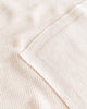 Close-up view of a textured Handmade Merino Wool Felix Blanket - Cream with fine horizontal ribs, neatly folded at one corner, showing details of its soft, plush material suitable for sensitive skin.