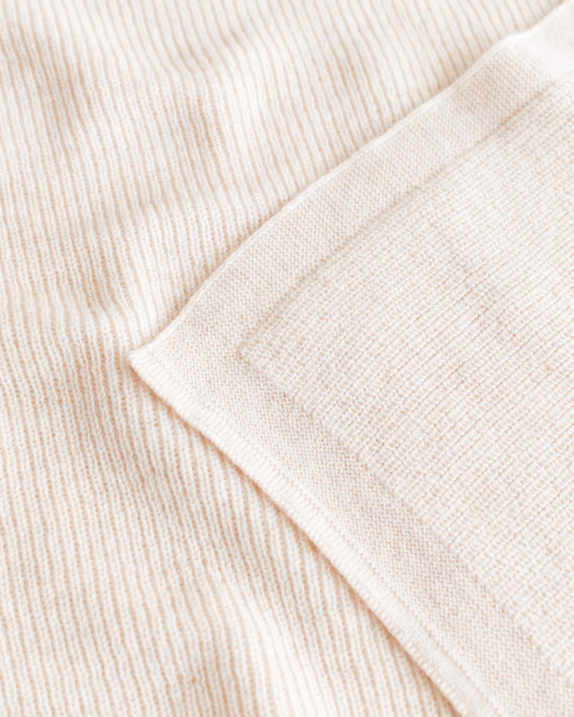 Close-up view of a textured Handmade Merino Wool Felix Blanket - Cream with fine horizontal ribs, neatly folded at one corner, showing details of its soft, plush material suitable for sensitive skin.