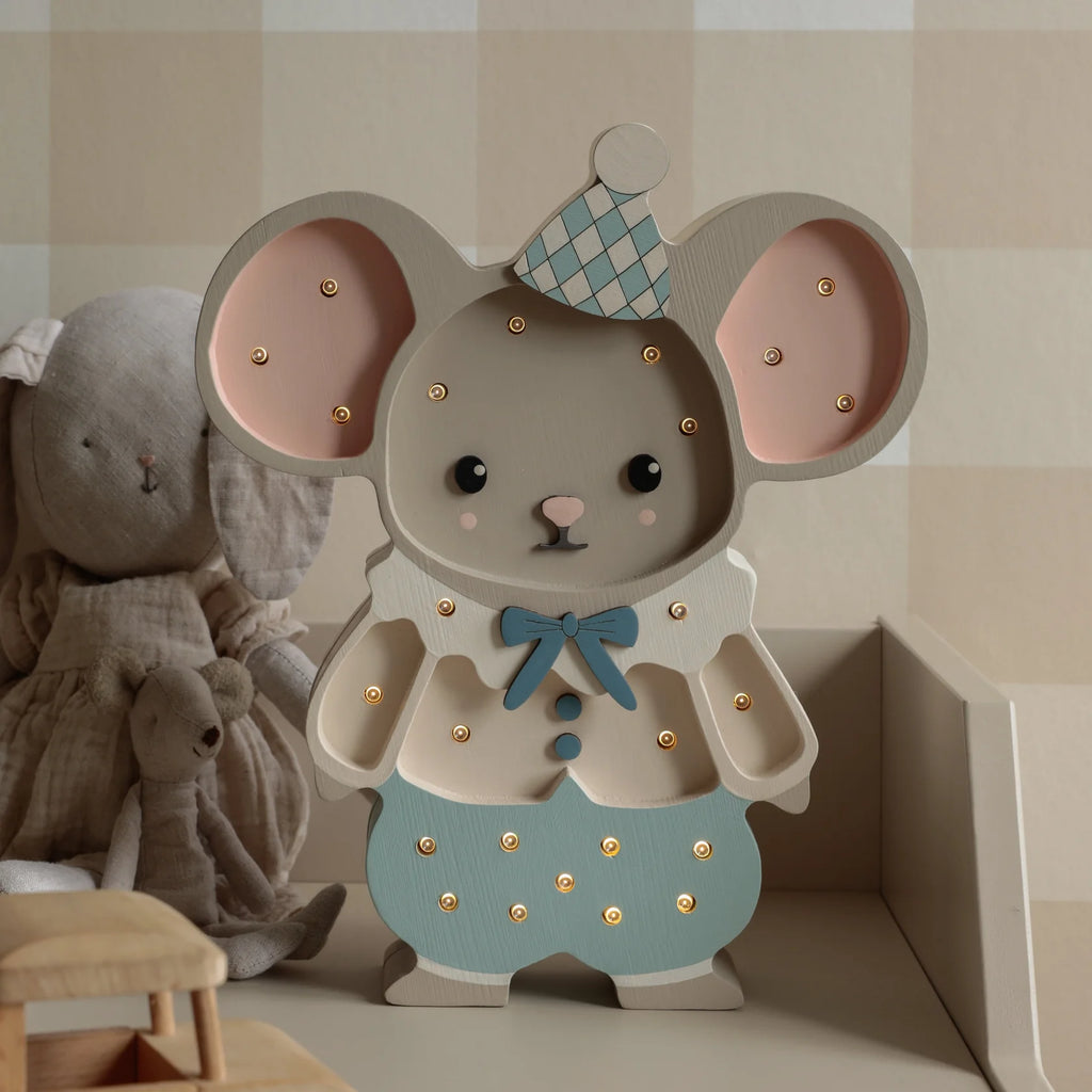 The Handmade Wooden Lamp - Felix The Mouse, crafted from pinewood and shaped like a mouse in a party hat, glows gently on a nursery shelf beside stuffed animals, adding warmth and charm to cozy children's decor.