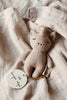 The Konges Sloejd Mini Unicorn Stuffed Animal, a soft light brown organic cotton baby toy with closed eyes, rests on pale textured fabric. Its round tag features "konges sløjd" and small triangle designs.