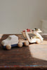 A Konges Sløjd Wooden Car Transporter made from FSC-certified beech wood rests on a sunlit table, with two small race cars placed on top. The minimalistic scene is warm, as natural light highlights the smooth curves of these delightful toys.