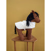 A Fabelab Friends Stuffed Animal - Horse Hector with a brown corduroy body and a fluffy white saddle, standing on a wooden stool against a yellow background.