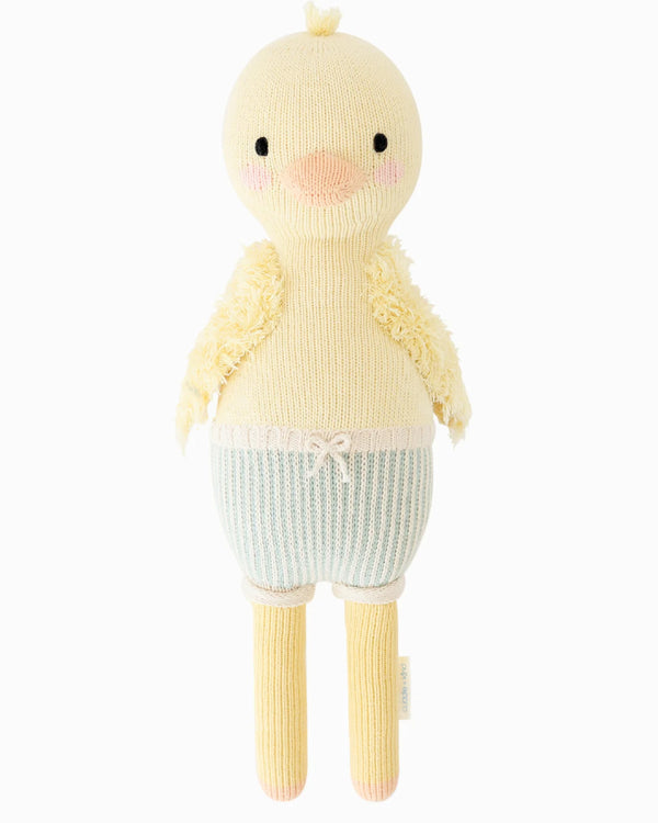 Cuddle + Kind Duckling is a cute, handmade yellow knit plush with a round head, blush cheeks, soft wings, long legs, pale blue and white striped shorts with a pink bow, and hypoallergenic polyfill stuffing.