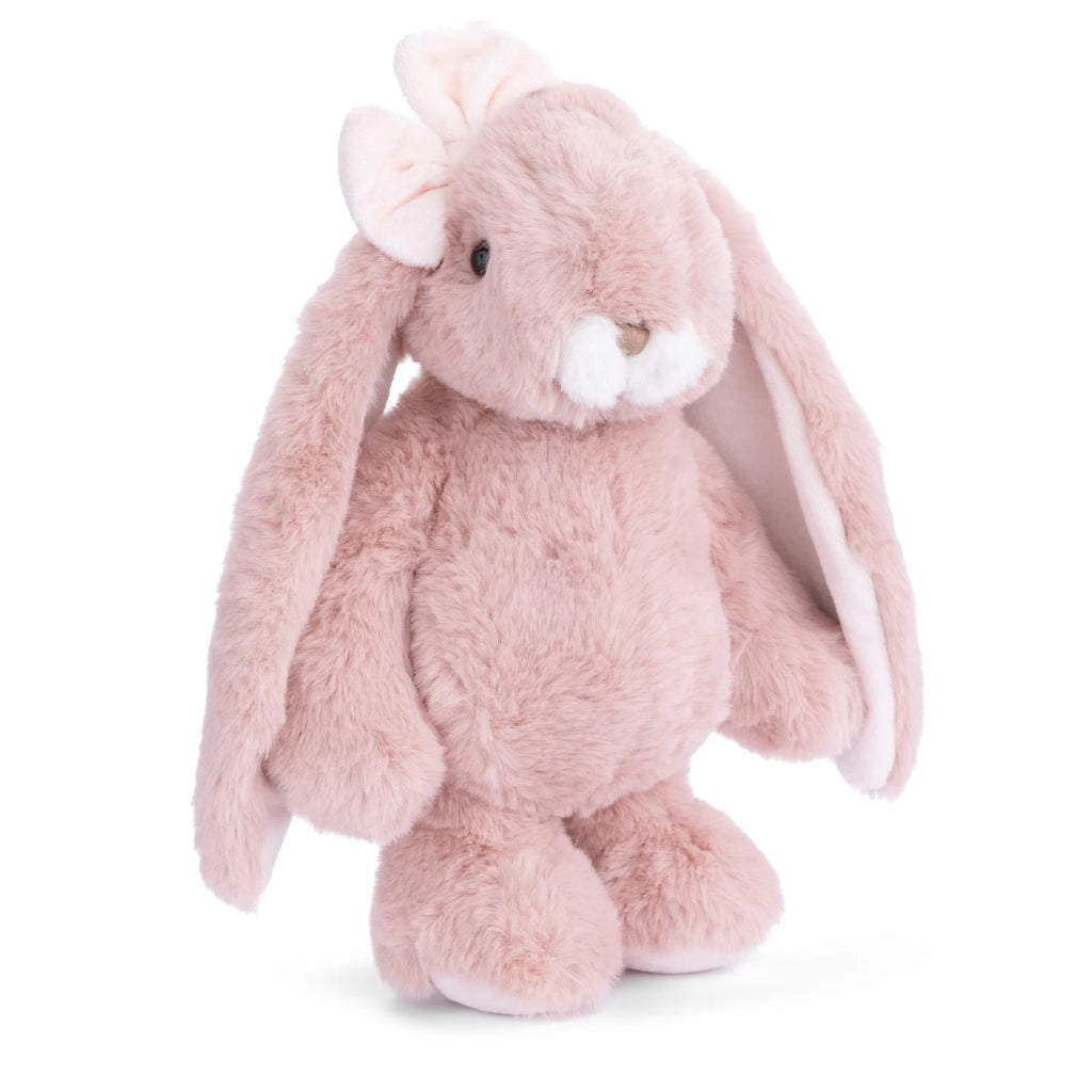 Standing upright against a white background, the Bukowski - Friendly Kanina - Antique Pink is a plush rabbit featuring an antique pink hue, long floppy ears, a small white nose, and a charming bow on one ear. This comforting stuffed animal is perfect for cuddling and makes an adorable companion, capturing the timeless appeal of the Friendly Kanina collection.