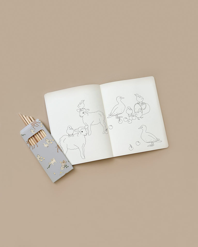 A "Coloring Book and Colored Pencils - Farm" lies open on a beige surface, revealing line drawings of various farm animals, including birds and a cow. Beside the coloring book is a matching set of decorative colored pencils, with one pencil partially out, inviting you to dive into this creative activity.