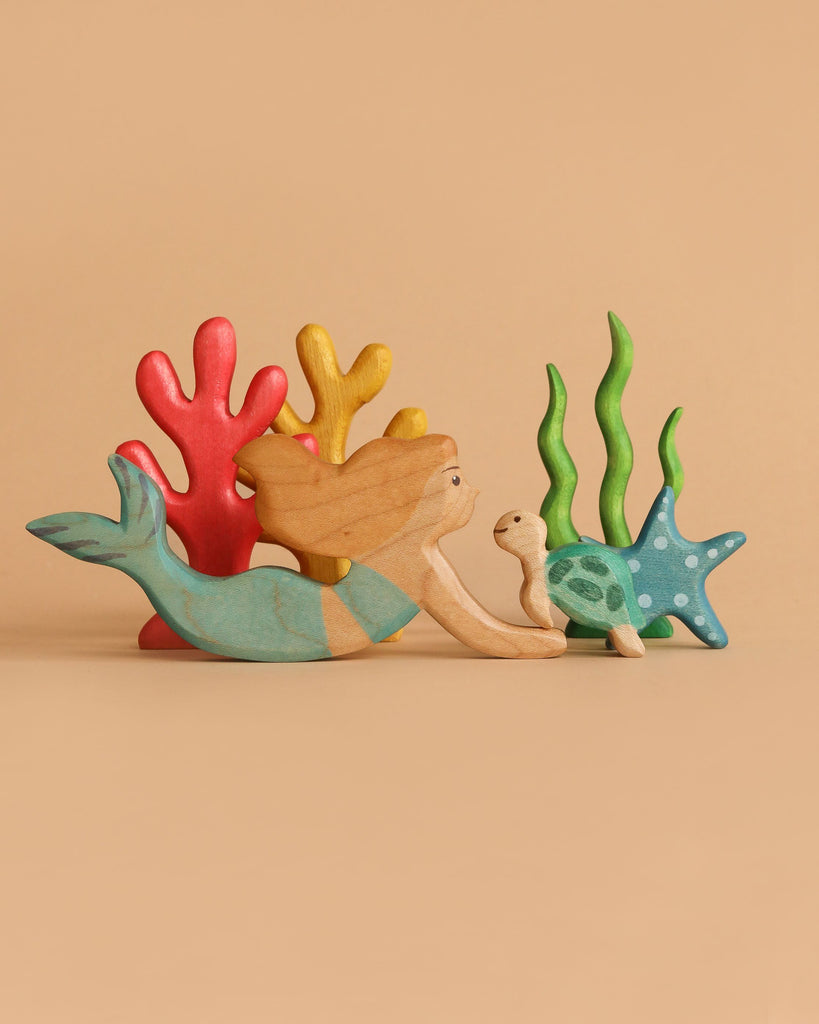 The Handmade Holzwald Mermaid Set features a wooden mermaid with long hair swimming beside a small turtle, surrounded by colorful coral and seaweed—an enchanting educational toy displayed on a beige background.