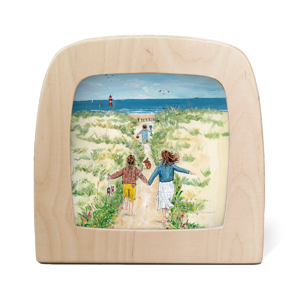 The "Silhouette Only - Sea" framed painting shows two children running hand in hand toward the beach, surrounded by sand dunes and grass under a bright blue sky. A lighthouse stands in the distance against the ocean backdrop. The frame is crafted from light wood with food-safe materials.