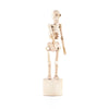 The Wooden Lazy Bones Skeleton Pop Up stands upright on a round wooden base, resembling a skeletal frame. The figure's limbs and joints are simplified and movable, giving it an articulated appearance. The light-colored wood is unpainted, showcasing the natural grain.