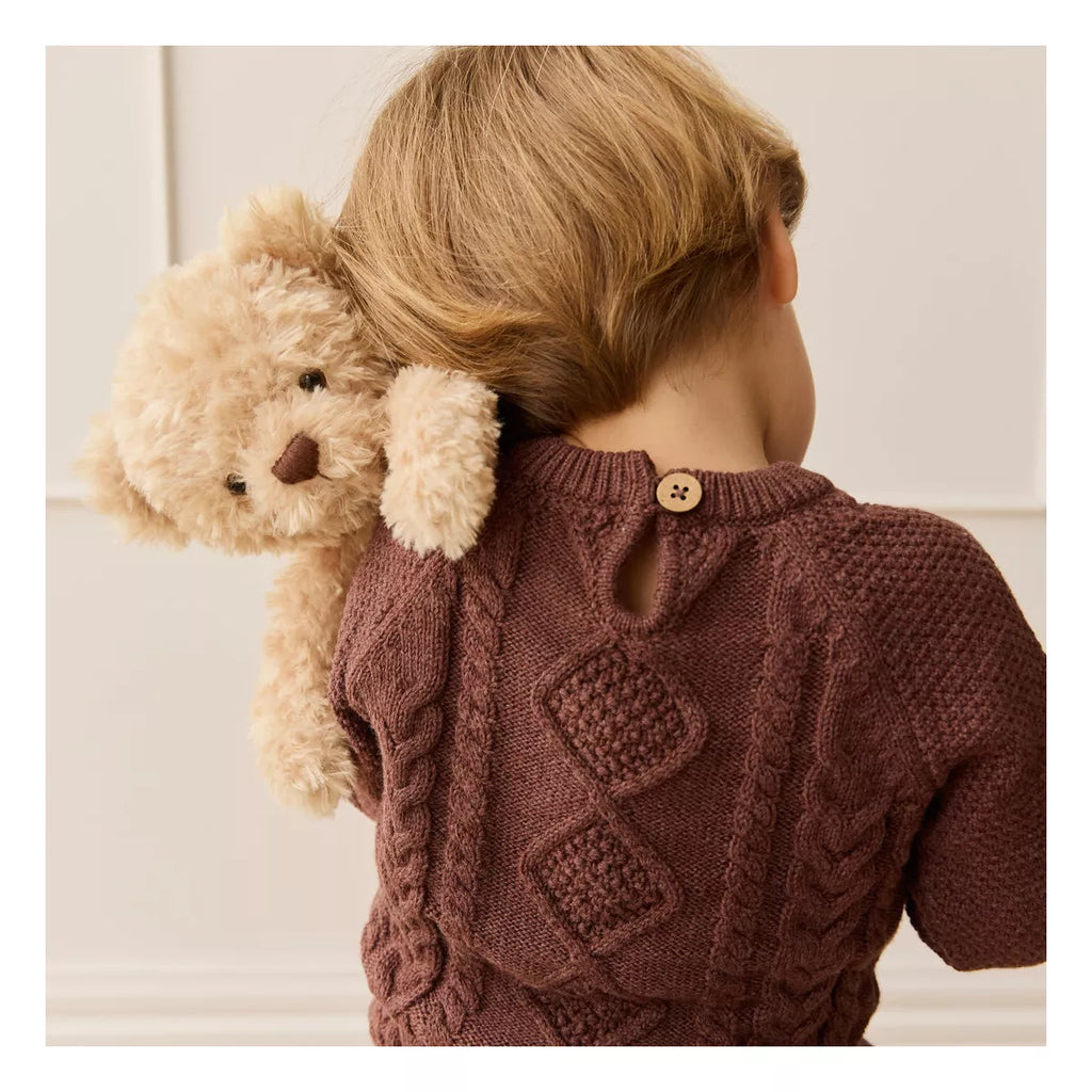 A young child with light brown hair, seen from behind in a brown knitted sweater, holds the Snuggle Bunnies - Arthur the Bear, made from super soft toys fabric, over their shoulder. Ships in approximately one week.
