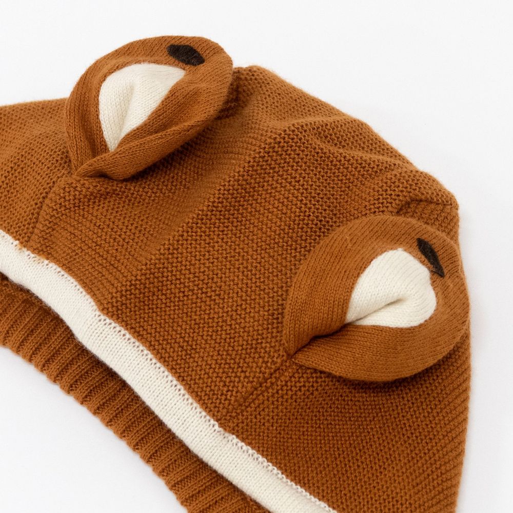 A brown knitted Meri Meri Fox Bonnet & Booties Set with bear ear details on the hood, featuring white and black accents inside the ears. The sweater has a visible white hem and is a perfect baby shower gift.