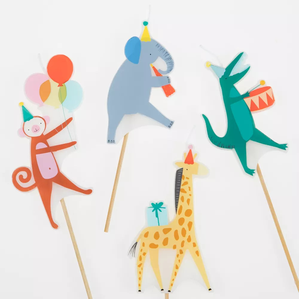 Four Meri Meri Animal Parade Candles on sticks for a birthday party cake, including a monkey with balloons, an elephant with a party hat, a dancing unicorn, and a giraffe holding a gift, against a