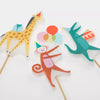 Meri Meri Animal Parade Candles depicting a giraffe, a cat with balloons, and a kangaroo with a drum, all mounted on sticks against a white background for a birthday party cake.