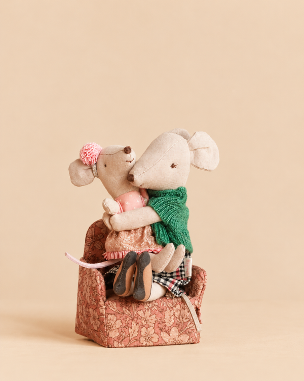 Two toy mice in clothing embrace while sitting in a small, patterned Maileg Grandma’s Hug chair.