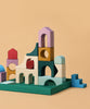 The Grimm's Small Building Set - Floors features vibrant wooden blocks in assorted shapes and sizes, stacked on a green base against a beige background, evoking abstract architectural designs.