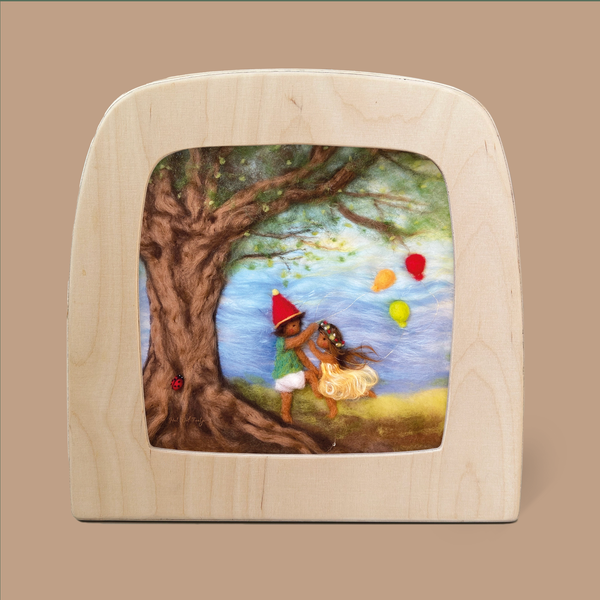 The "Silhouette Only - We Celebrate The Seasons for Toverlux Lamp" features a charming felt artwork depicting two children joyfully dancing by a majestic tree, creating the warmth of a cozy home. The child on the left is adorned with a pointed red hat, and the one on the right wears an elegant yellow dress. Enchanting silhouettes of vibrant balloons float gracefully against the tranquil scene.