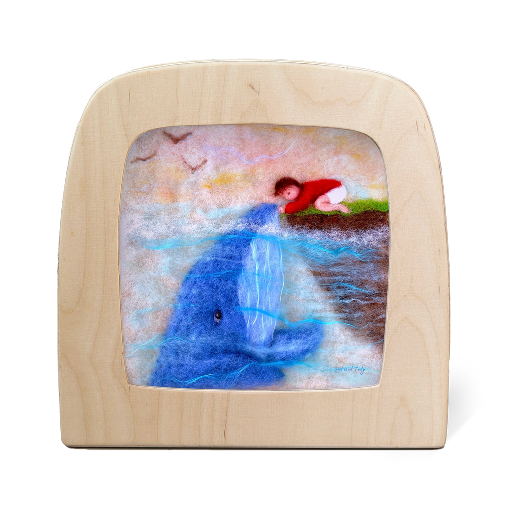 The felt art piece, "Silhouette Only - Whale Friend for Toverlux Lamp," depicts a child in a red sweater lying on grass and reaching toward a blue whale surfacing from the water, with birds flying above. This enchanting scene is framed in a wooden, TV-shaped frame to charm any home atmosphere.