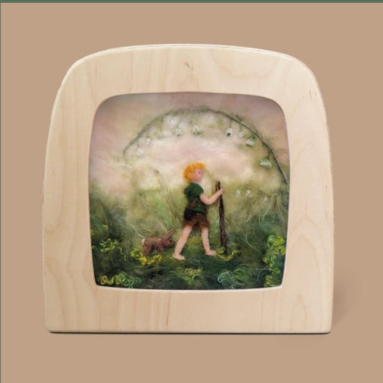 A felt artwork titled "Silhouette Only - Little Explorer" captures a person with orange hair and a dog walking through a misty green landscape. Surrounded by swirling plants, they hold a staff, creating magical silhouettes in the haze. The piece is elegantly showcased in a light magic window frame and ships in approximately one week.