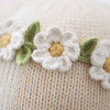A close-up of Cuddle + Kind Hannah the Bunny's cream-colored premium cotton yarn fabric, adorned with crocheted white flowers featuring yellow centers and green leaves.