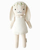 Cuddle + Kind Hannah the Bunny is a cream-colored hand-knit bunny doll with long floppy ears, dressed in a white dress and daisy flower crown. Made from premium cotton yarn, this fair trade bunny has black eyes, pink cheeks, and a sweet smile.