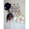 A black riding hat is hung on a wall-mounted coat rack with wooden knobs. Next to it, there's a brown Hobby Horse with a blue bridle and black mane. A white quilted bag made of organic cotton by Fabelab, adorned with a horse print, hangs on the same rack.