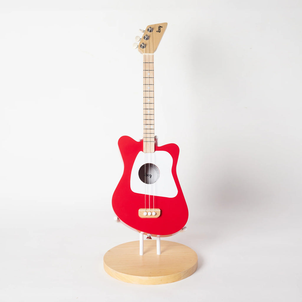 A red Loog Mini guitar with a white center, mounted upright on a circular wooden Guitar Stand For Loog Mini against a plain white background.