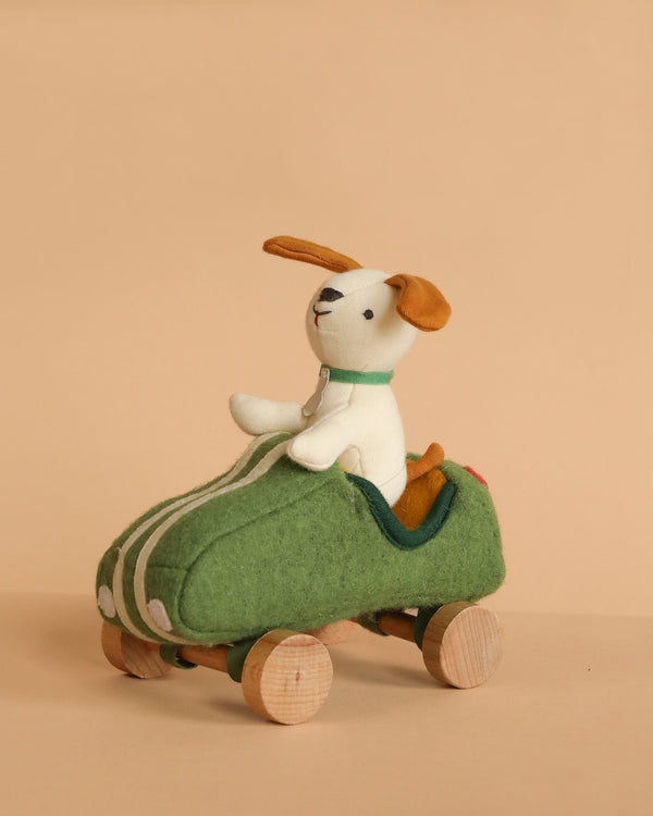 The Olli Ella Holdie Dog-Go - Racer Boy - Green features a stuffed toy dog with floppy brown ears riding in a green felt shoe on wheels, perfect for imaginative play or as a cute nursery decoration.
