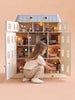 A young child kneels and plays with the House of Monaco — The Grand Mansion, a fully furnished dollhouse with lights featuring illuminated rooms and miniature furniture inspired by Haussmann-style elegance, all set against a plain beige background.