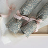 two cylinder shaped objects gift wrapped in blue floral wrapping paper fastened with dusty pink ribbon.