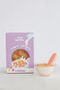 A purple box labeled "Tiny Harlow Tiny Loops Cereal" stands beside a Tiny Tummies - Tiny Loops Cereal Bowl filled with colorful loops and a pink spoon, perfect for doll breakfast play, set against a simple light background.