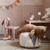 A cozy children's room with pastel decor, featuring a stuffed bear on the Maileg Drum Pouf, a pastel chair with a soft toy, a small table with a lamp and toys, and a colorful pennant banner on the wall.