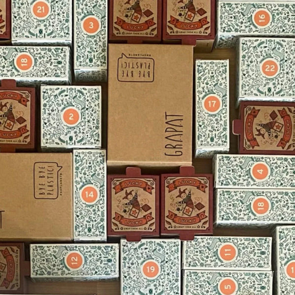 A collection of stacked Grapat Advent Calendar boxes with various labels and numbers in a disorganized arrangement, featuring vintage-style graphics on the visible sides, recommended for ages +36 months.