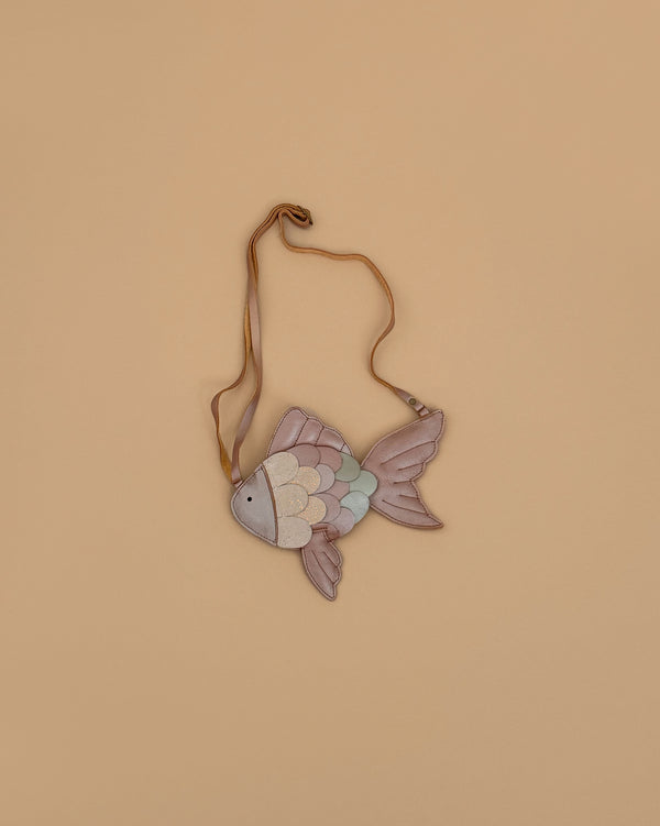 The Donsje Leather Thysa Purse - Gold Fish, a small fish-shaped bag with pastel scales and a tan adjustable strap, is displayed against a beige background.