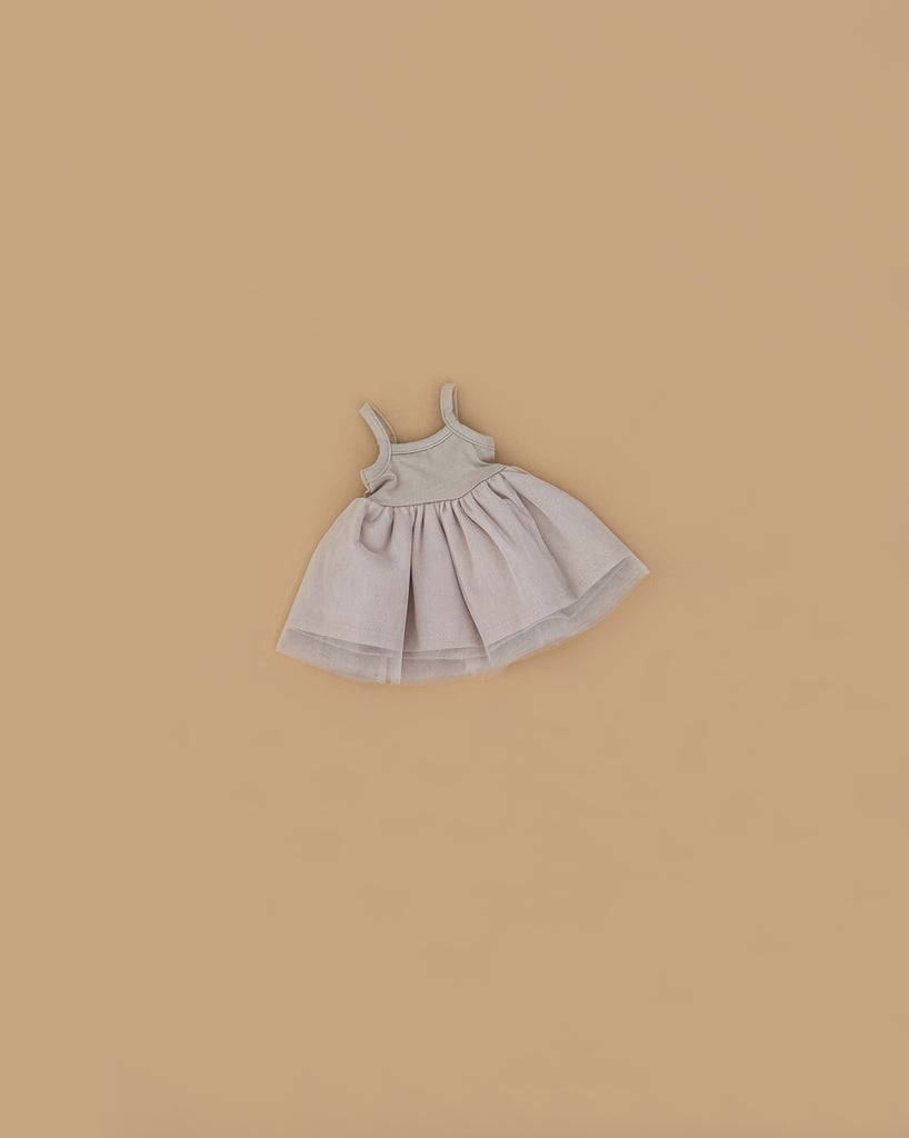 The Minikane Doll Clothing | Rosella Tutu - Pink, a small sleeveless light pink dress with a fitted bodice and flared skirt, designed in France for Minikane dolls, is laid flat on a plain beige background.