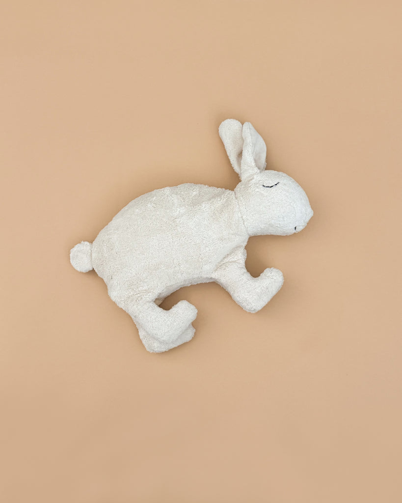 A soft Senger Naturwelt Cuddly Animal - White Bunny with closed eyes lies on its side against a plain beige background, evoking cozy charm.